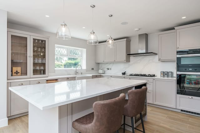 Light kitchen with a white island, glass pendants, upholstered stools and timber flooring